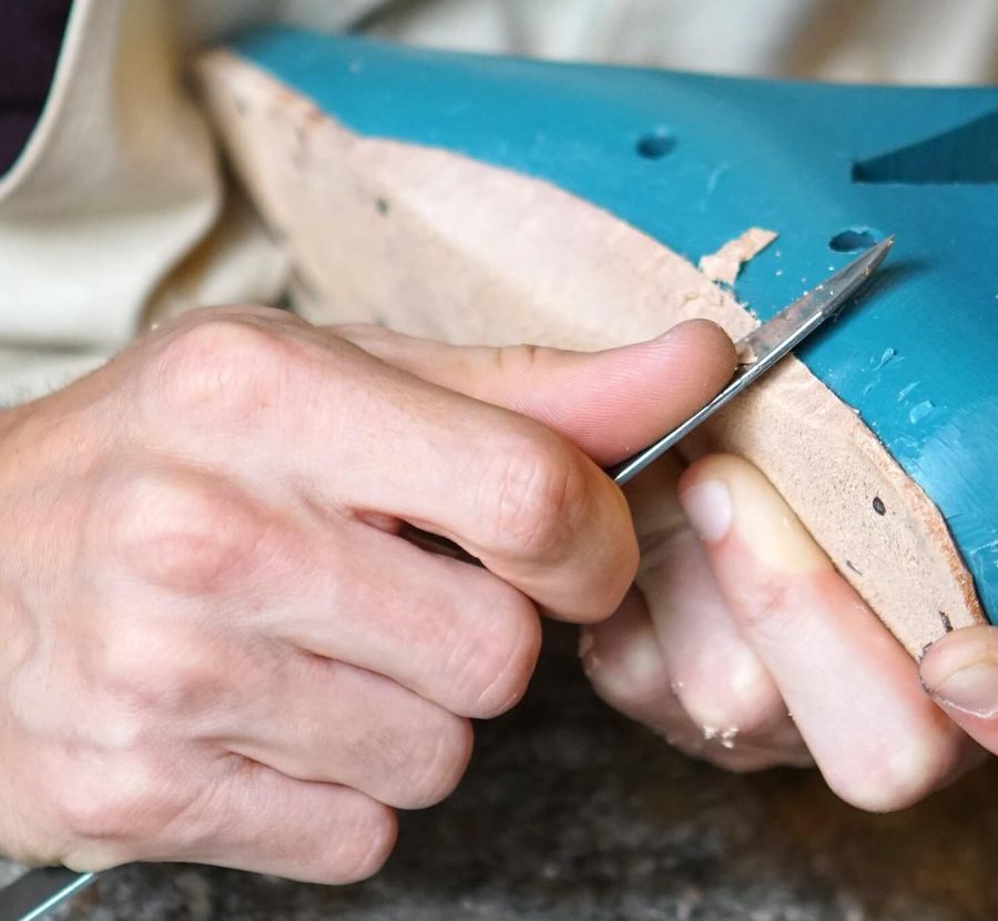 Shoemaker's hands trimming a leather insole on a shoe last